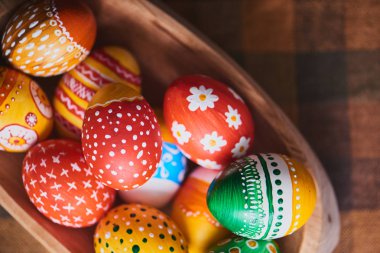 Damalı masa örtüsü arka plan üzerinde renkli boyalı Paskalya yığını ile ahşap kase yumurta 