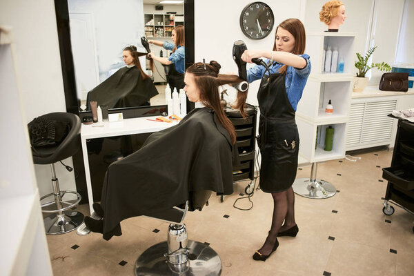 professional hairdresser in process of drying clients hair with hairdryer at barber