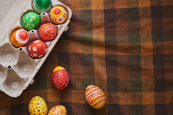 painted eggs with patterns in cardboard container on checkered tablecloth, Easter holiday concept