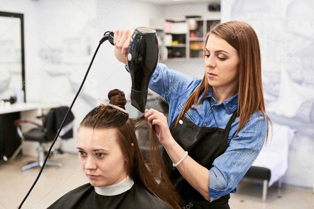 professional hairdresser in process of drying clients hair with hairdryer at barber