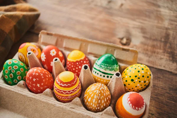painted eggs with patterns in cardboard container with checkered tablecloth on wooden background, close-up , Easter holiday concept