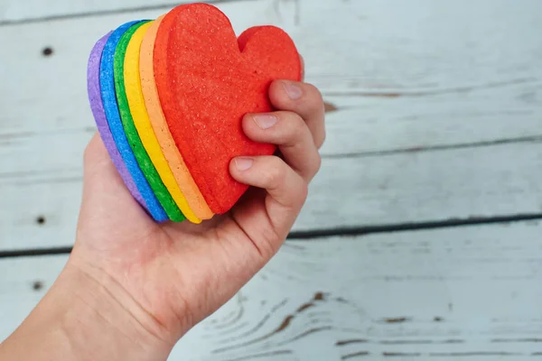male hand holding hearts painted in rainbow colors on wooden background , LGBT concept