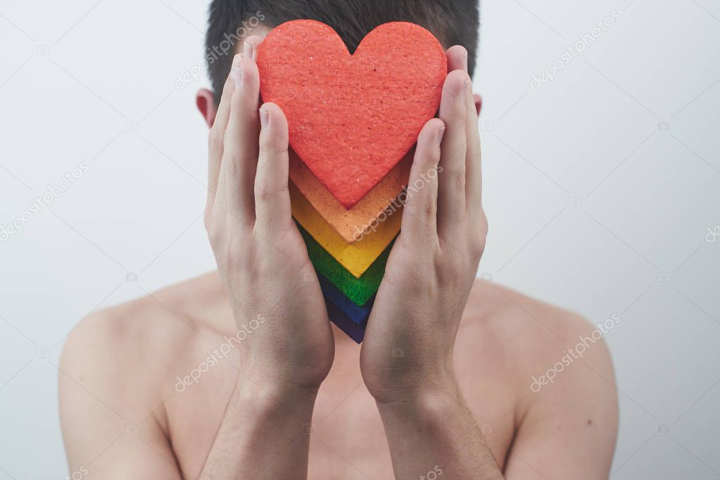 gay guy holding in hands hearts in colors of rainbow in front of face, LGBT community concept 