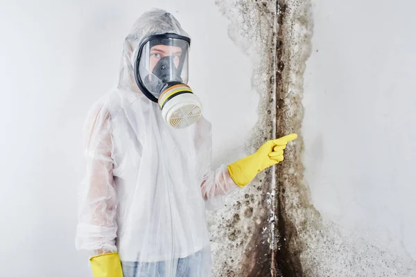 一个专业的消毒器在工作服和面具指向墙上的黑色模具的手指 去除公寓和房子中的真菌 — 图库照片