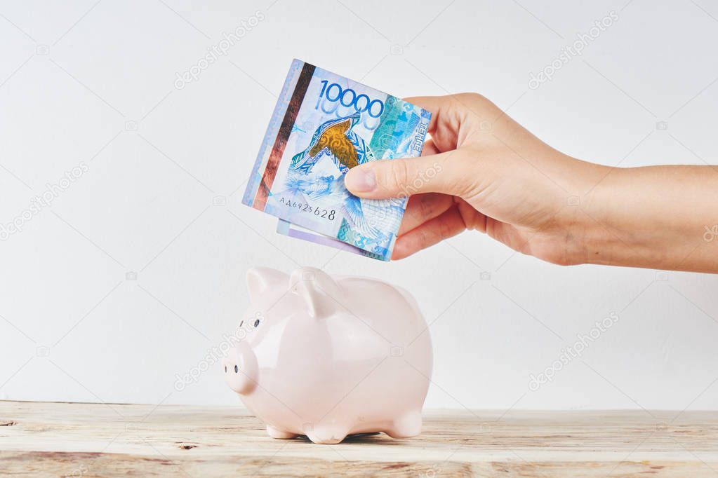 female hand puts Kazakh money in a piggy bank on a white background