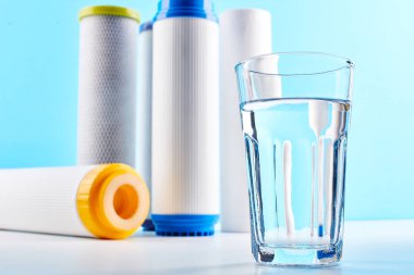 Su filtreleri. Karbon kartuşlar ve beyaz mavi arka planda bir bardak. Ev filtreleme sistemi.
