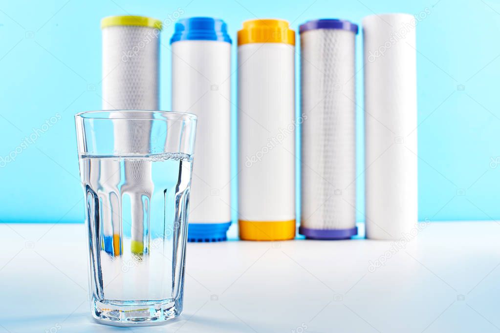 Water filters. Carbon cartridges and a glass on a white blue background. Household filtration system.