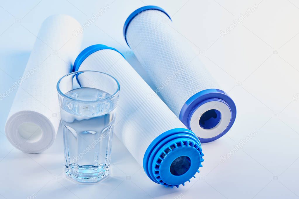 Water filters. Carbon cartridges and a glass on a white background. Household filtration system.