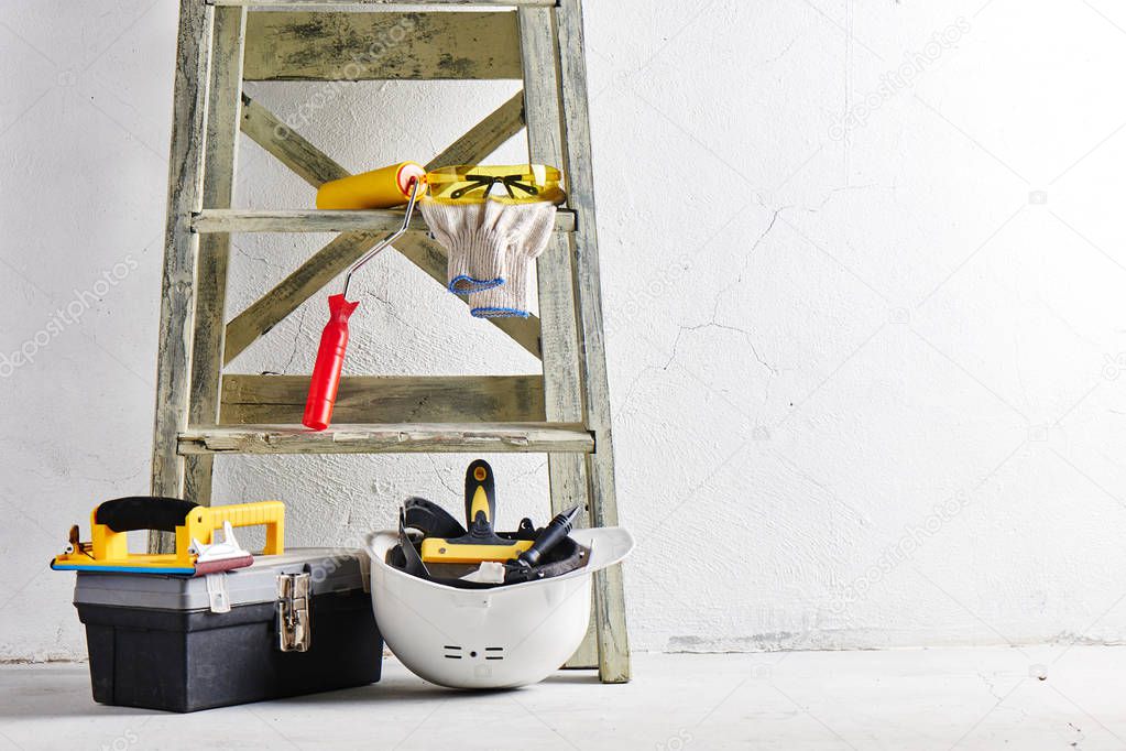 Construction tools and stepladder on a white wall background. Repairs