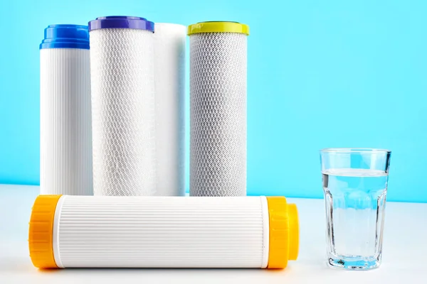 Water filters. Carbon cartridges and a glass on a white blue background. Household filtration system.