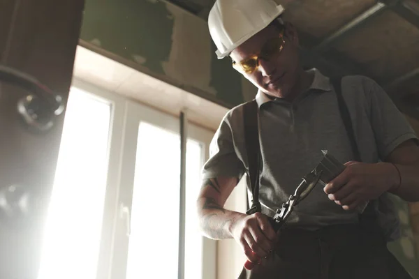 Worker cutting profile for drywall against window at building, concept of room repair