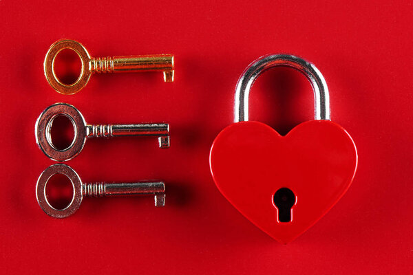 The concept of female infidelity. A heart shaped lock and three keys to it on a red background.
