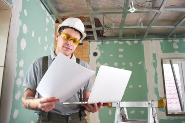 Oda onarım. Bir dizüstü bilgisayar ve çizimler inşaat zemin üzerine onun elinde Oluşturucusu'nda kask ve gözlük standları