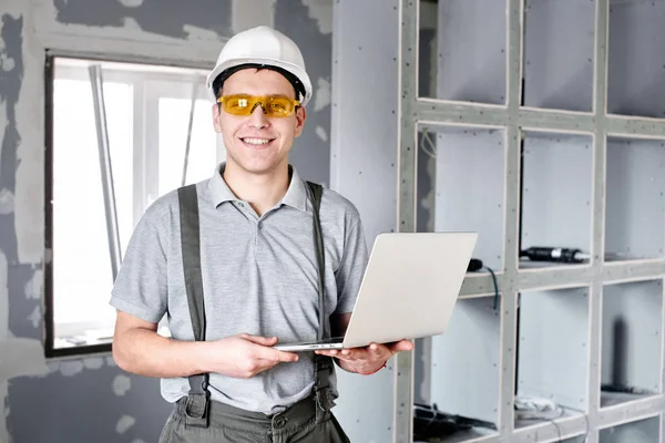 Oda onarım. İnşaat arka plan üzerinde elinde bir dizüstü bilgisayar ile Oluşturucusu'nda kask ve gözlük standları