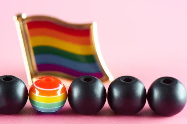 The concept of the LGBT community. A lot of black balls and one multicolored on the background of the rainbow flag.