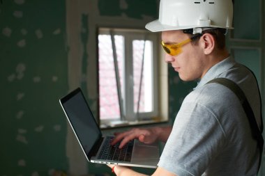 Oda onarım. İnşaat arka plan üzerinde elinde bir dizüstü bilgisayar ile Oluşturucusu'nda kask ve gözlük standları