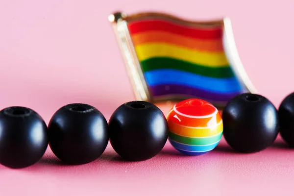 The concept of the LGBT community. A lot of black balls and one multicolored on the background of the rainbow flag.
