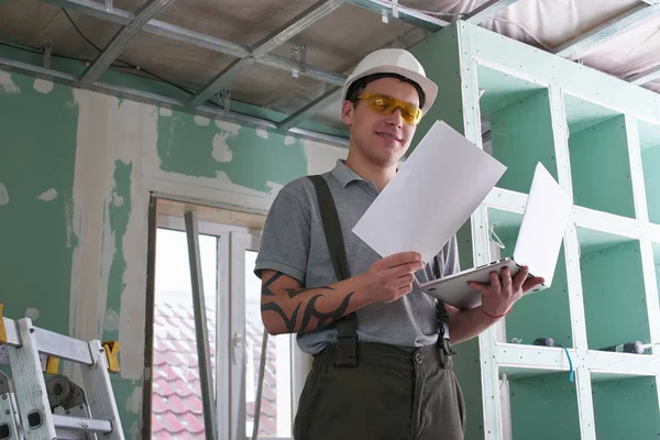 Room Repair Builder Helmet Glasses Stands Laptop Drawings His Hands — Stock Photo, Image