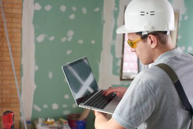 Oda onarım. İnşaat arka plan üzerinde elinde bir dizüstü bilgisayar ile Oluşturucusu'nda kask ve gözlük standları