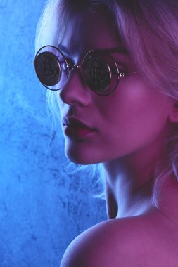 Bitcoins kırmızı mavi sesi ile gözlük kırmızı dudaklar ile güzel bir genç sarışın kadının profili. Cryptocurrency kavramı. Yaratıcı neon aydınlatma