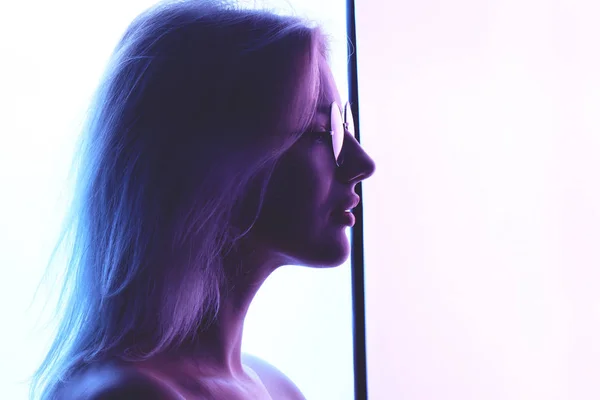 青いネオンが創造的な照明の背景にガラスと美しい若い金髪女性のプロフィール — ストック写真