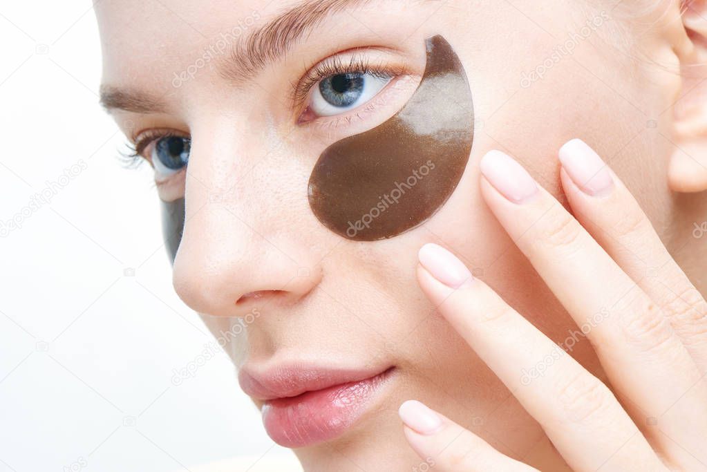 Beautiful young blond woman shows fingers on eye patches of black color on a white background in isolation. Care and face masks