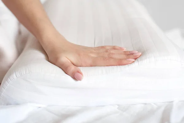 Female hands hold and show an orthopedic pillow on a white bed. Comfortable sleep and healthy spine
