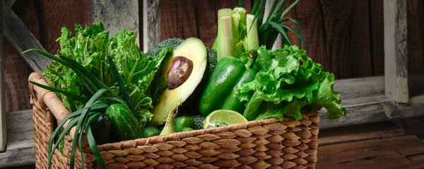 Green vegetables and fruits and greens in a brown wicker basket on a wooden background. Healthy eating concept