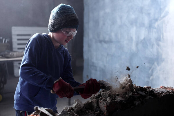 Little boy the son of worker, helps his father to break brick wall with hammer, repairs his house, building