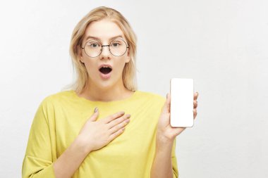 Şok Avrupa sarışın kadın gözlük, mobil telefon elinde, sürpriz, ekranda, gördükleri gelen duygular içinde şişkin gözler çene düştü tutar. Güzel kız beyaz izole portresi 