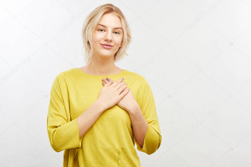 Loyalty and dedication to partner concept. Cute, contented smiling girl holds both palms on heart, promises to be honest makes thankful gesture on white background