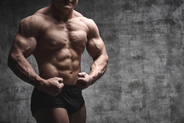 Seksi vücut geliştirmeci adam siyah şort koyu arka plan üzerinde poz. Yakışıklı pompalanan erkek vücudu reklam için boş alan ile izole