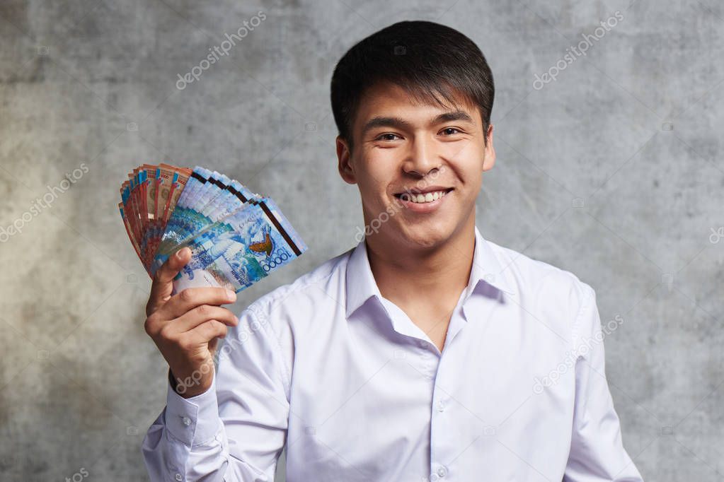 Asian businessman with bunch of Kazakh tenge in hand. Successful entrepreneur has earned a lot of money on transactions and sale of stock.