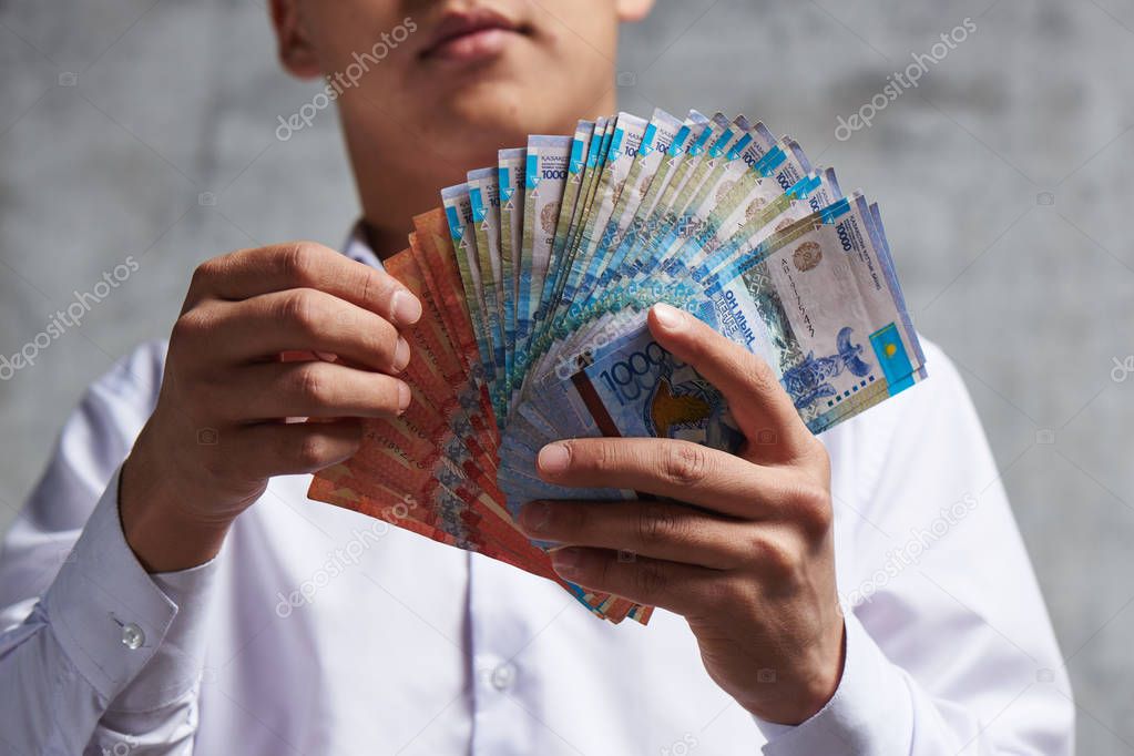 Asian businessman with bunch of Kazakh tenge in hand. Successful entrepreneur has earned a lot of money on transactions and sale of stock.