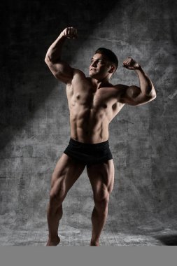 Seksi vücut geliştirmeci adam siyah şort koyu arka plan üzerinde tam büyüme poz. Yakışıklı pompalanan erkek vücudu reklam için boş alan ile izole