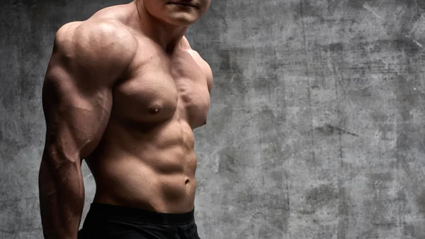 Seksi vücut geliştirmeci adam siyah şort koyu arka plan üzerinde poz. Yakışıklı pompalanan erkek vücudu reklam için boş alan ile izole