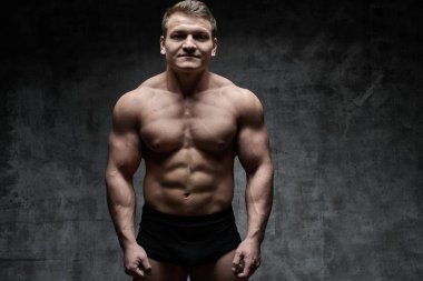 Seksi vücut geliştirmeci adam siyah şort koyu arka plan üzerinde poz. Yakışıklı pompalanan erkek vücudu reklam için boş alan ile izole