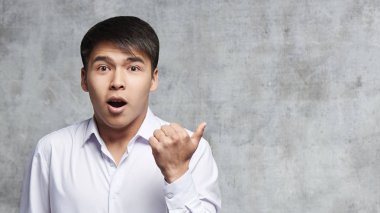 Asyalı iş kıyafetleri bir şey reklamını. Genç Kazak sürpriz neşeli yüz ifadesi ile ürün için boş alan tarafında parmak.