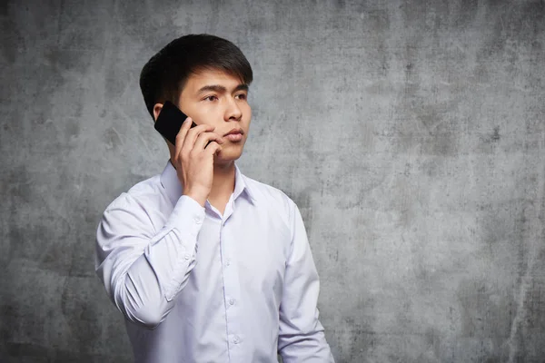 Portrait of a young Kazakh man talking on the phone with a serious facial expression against a gray studio background