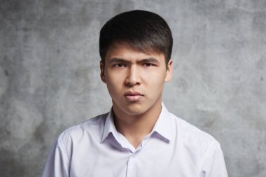 Kötü yüz ve gri arka plan üzerinde kaşlarını kaşlarını ile Ciddi Asya öğrenci. Duygusal Kazak kamera da hoşnutsuzluk ile görünüyor