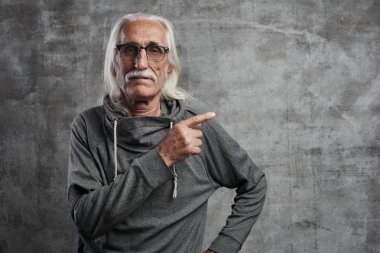 Yaşlı gri saçlı Kafkas adam işaret parmağı ile yan işaret, bir şey reklamı. Bıyıklı gözlüklü büyükbaba ürününüzü satın almanızı önerir 