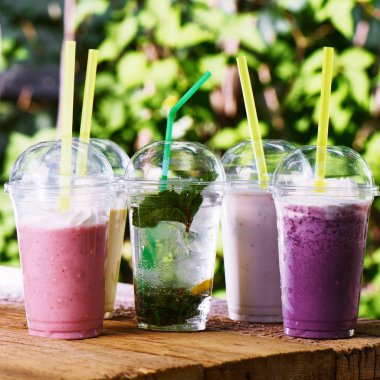 Serinletici alkolsüz renkli içecekler, kremalı süt lütfiti kokteyli, mojito, buzlu çay. Yaz barda saman ile plastik cam Milkshake, doğa arka plan 