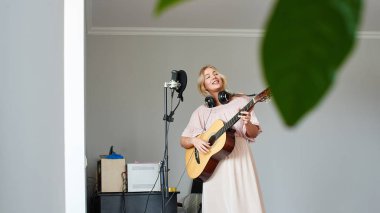 Ev kayıt stüdyosu bir gitar ile kulaklıklar güzel sarışın şarkıcı kız bir mikrofon içine bir şarkı söylüyor