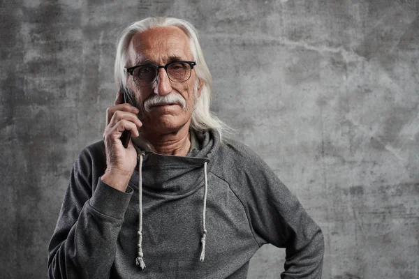 Gözlüklü eski bir gri Beyaz dede stüdyoda gri bir arka plan üzerinde ciddi bir yüz ifadesi ile telefonda konuşurken