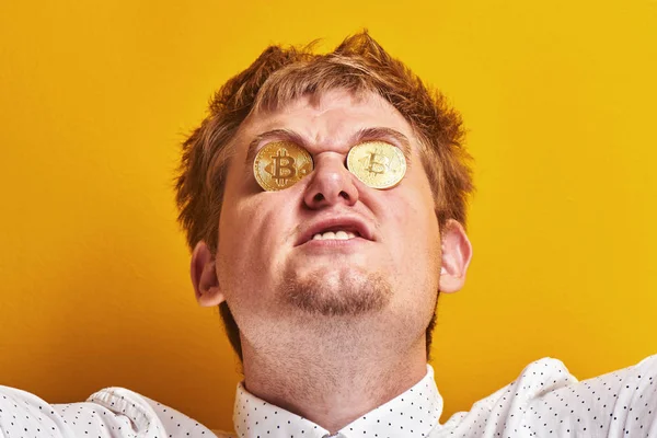 Portait of funny fat man with sinister face, bitcoins in the eyes on yellow background. Concept of virtual digital money, greed, vanity, wealth and stinginess