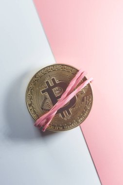 Fiziksel altın sikke bitcoin pembe beyaz arka plan üzerinde para için bir lastik bant ile sıkılır. Dijital kripto para birimi kavramı