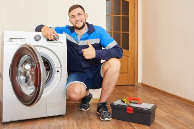 Tulumlu tesisatçı, evdeki çamaşır makinesini tamir ediyor.