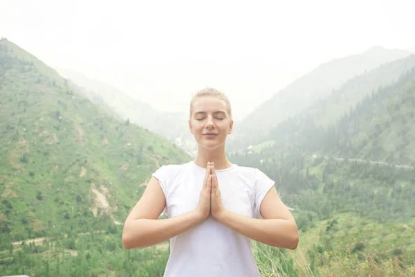 Sport girl doing yoga in mountains beautiful landscape. Young pacified woman leads  healthy lifestyle, meditates, relaxes namaste pose in bright sportswear on nature