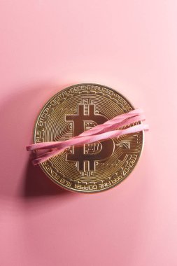 Fiziksel altın sikke bitcoin pembe bir arka plan üzerinde para için bir lastik bant ile sıkılır. Dijital kripto para birimi kavramı
