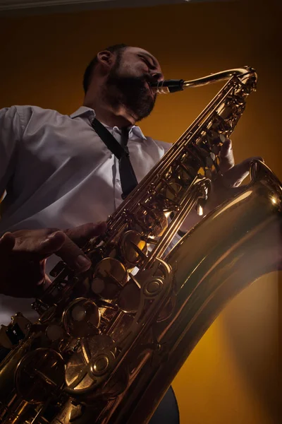 专业音乐家萨克斯管演奏家在白色衬衫的肖像演奏爵士音乐萨克斯管 黄色背景在摄影棚 底部视图 — 图库照片